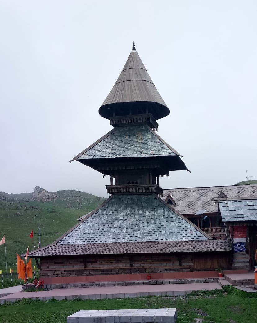 The three-tiered pagoda-style Parashar Rishi Temple at Prashar Lake, slate roof, deodar wood walls, prayer flags fluttering at the base
