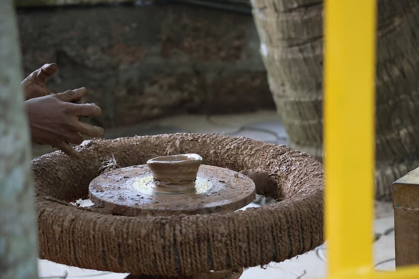 Hands reaching toward a spinning potter's wheel with a small clay pot forming, wet clay everywhere