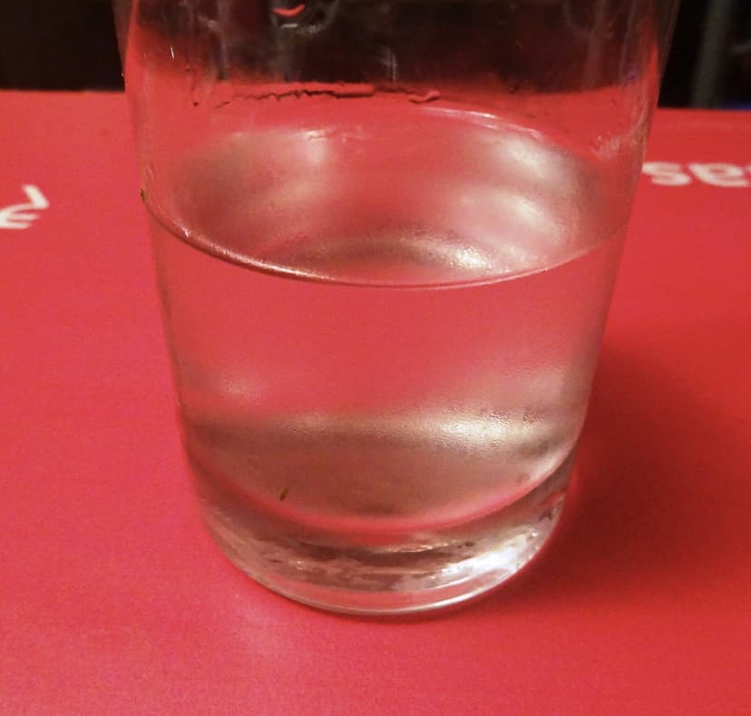 A short glass of clear urrak, the mild first-distillation cashew spirit, on a red table in Goa