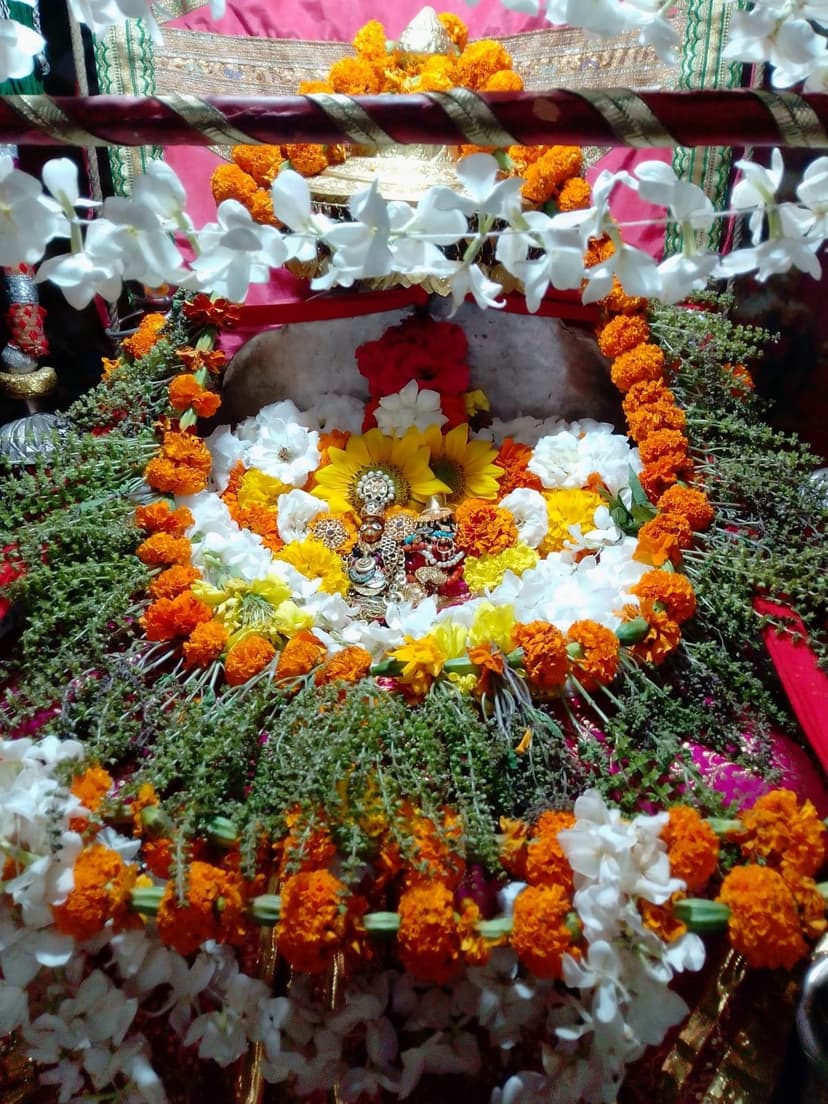 A small golden deity idol dressed in marigold and white chrysanthemum flowers