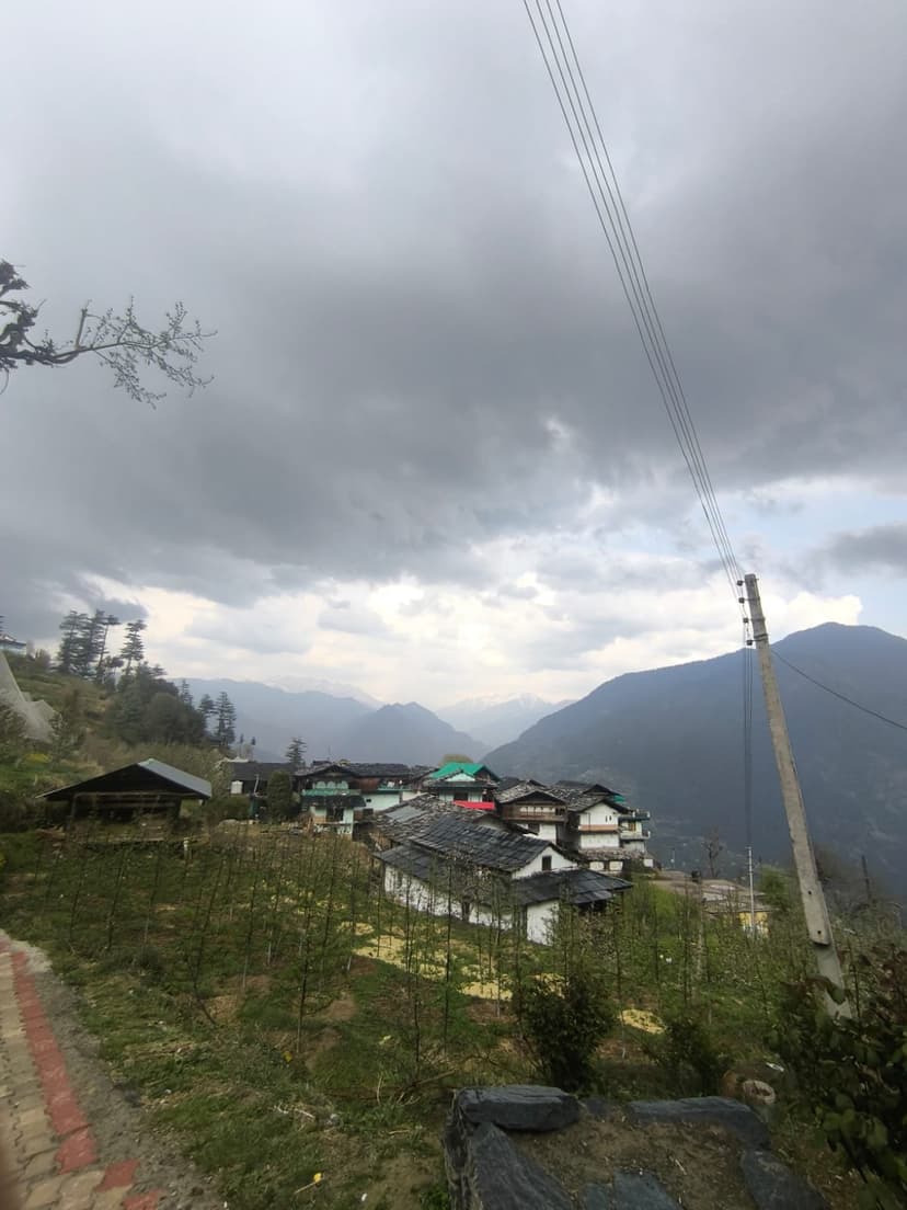 Hillside village with traditional houses on a steep slope under cloudy skies in Banjar area, Kullu district