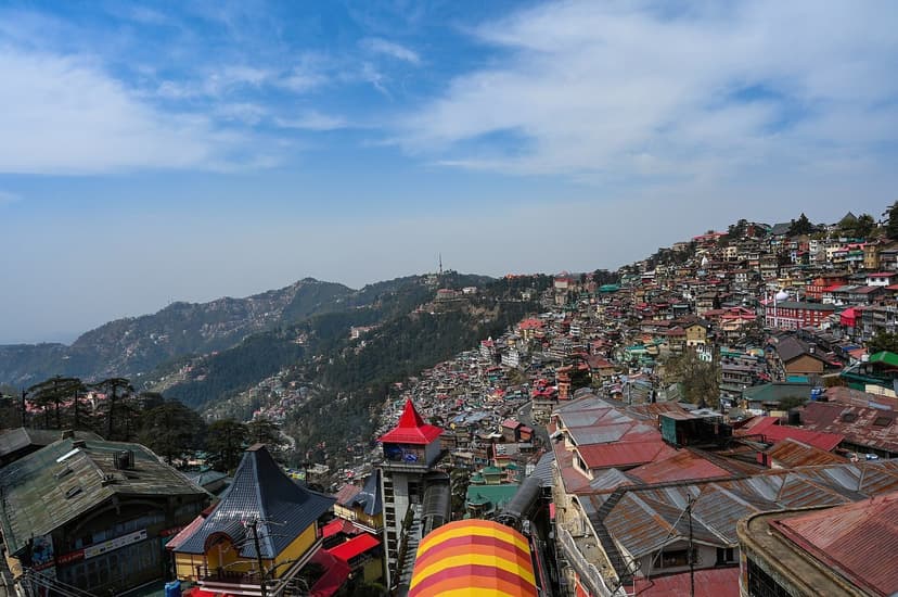Shimla cityscape with houses clinging to ridge, deodars, distant hills