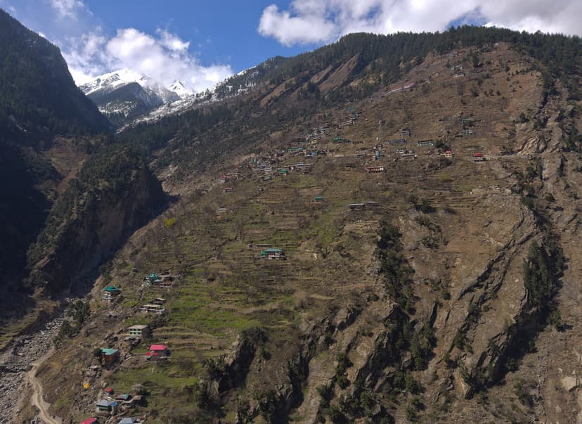 Brua village hugging a steep terraced hillside above the Baspa river in Sangla Valley Kinnaur, snow peaks visible upper left, scattered apple terraces
