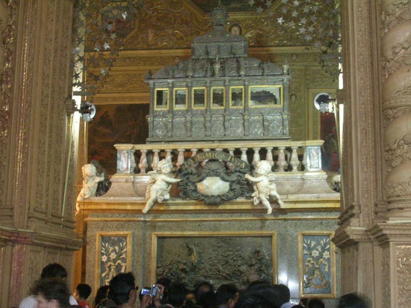 The ornate silver casket of St Francis Xavier raised high on a carved marble plinth with cherubs inside the gilded Basilica of Bom Jesus, a crowd of pilgrims below