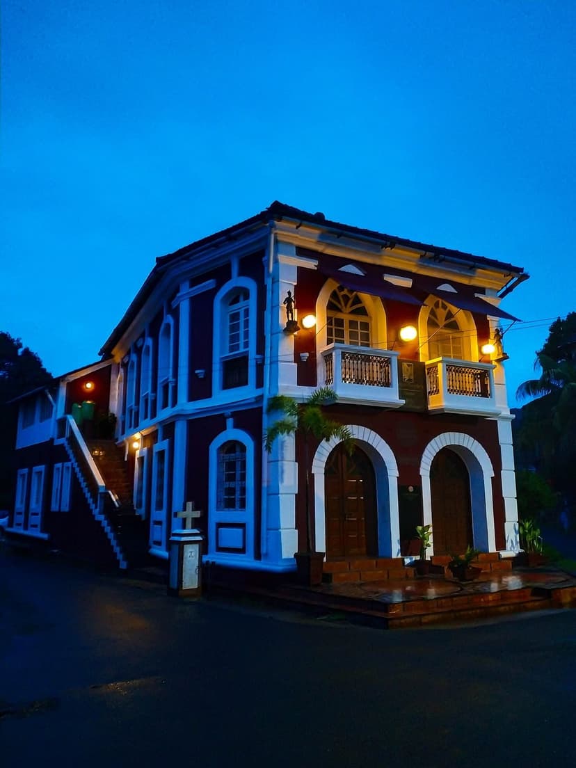 A restored Portuguese-era heritage house in Fontainhas, Panjim, its white-trimmed facade and balcony warmly lit at dusk against a deep blue sky.