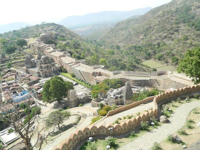 Elevated view of Kumbhalgarh Fort near Udaipur, its long fortified wall snaking down the green Aravalli hillside past temples inside the complex.