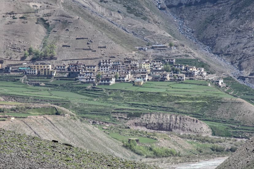 Wide shot of Mud village in Pin Valley, Spiti — cluster of stone houses below a dramatic mountain face