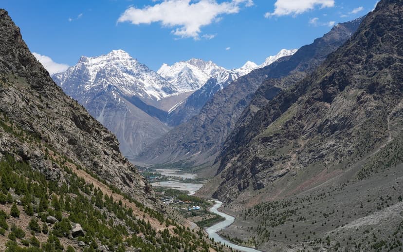 Bhaga river curving through a wide bare-rock Lahaul valley between the Darcha and Gemur settlements, snow peaks at the head of the valley and scattered village roofs below