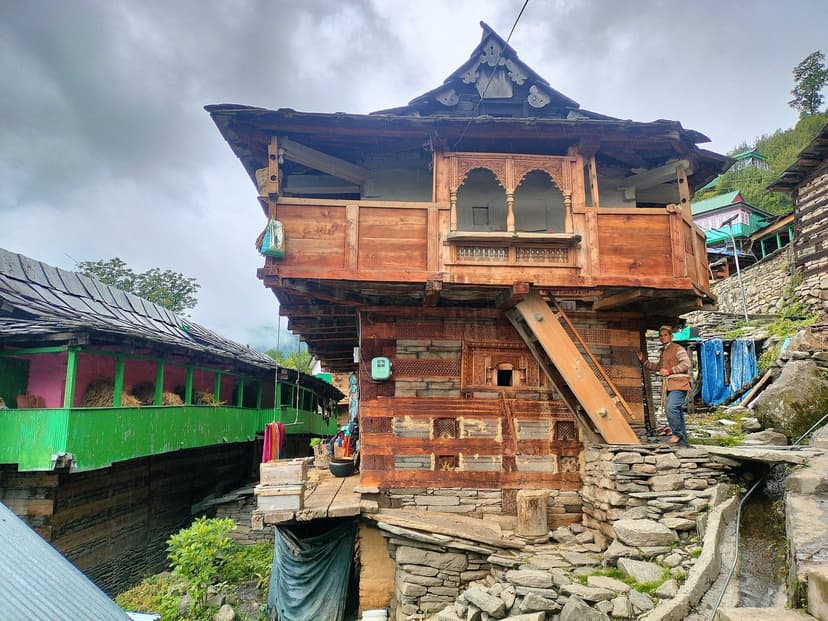 A lived-in traditional wooden village house with a carved balcony in Himachal Pradesh