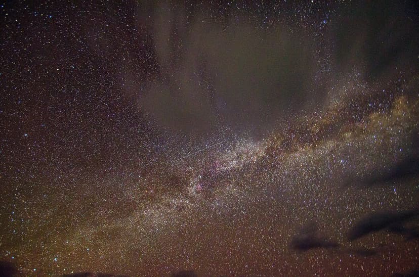 Close-up of the Milky Way galactic core with dust lanes and a single meteor streak crossing the frame