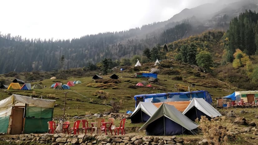 Tents pitched on the Kheerganga-area meadow with shepherd huts and misty forested peaks, before the camping ban