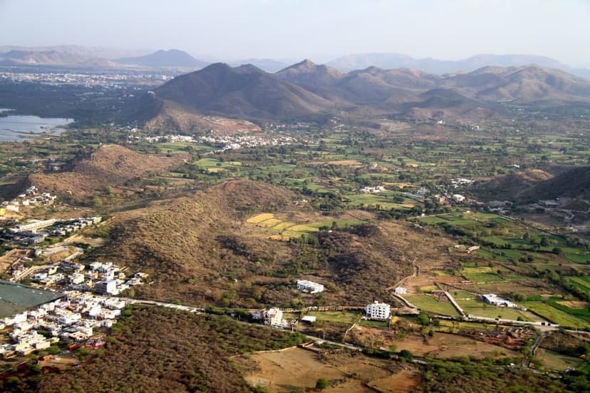 A high view over the Aravalli countryside around Udaipur, low hills, green farms, scattered villages and a lake in the distance