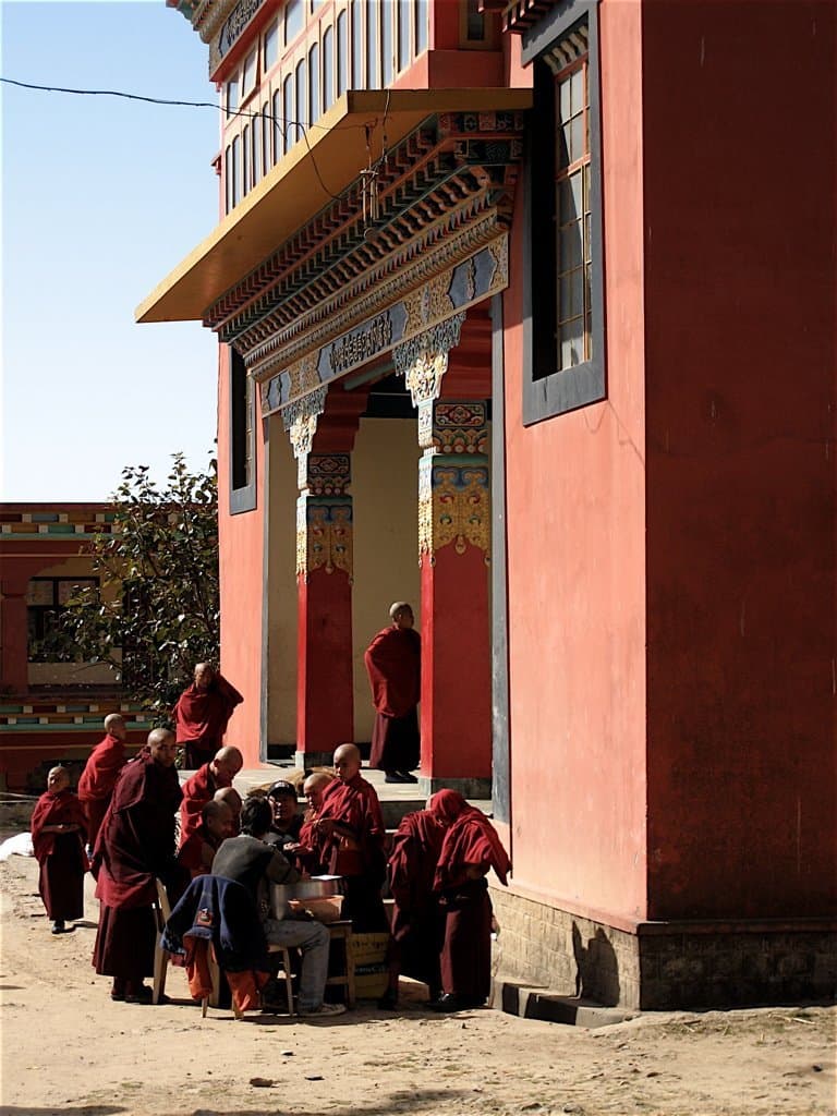 Monks gathered outside a red Tibetan prayer hall in Bir Tibetan Colony