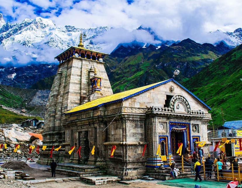 Kedarnath temple stone facade with prayer flags and snow-streaked peaks of the Kedarnath massif rising behind