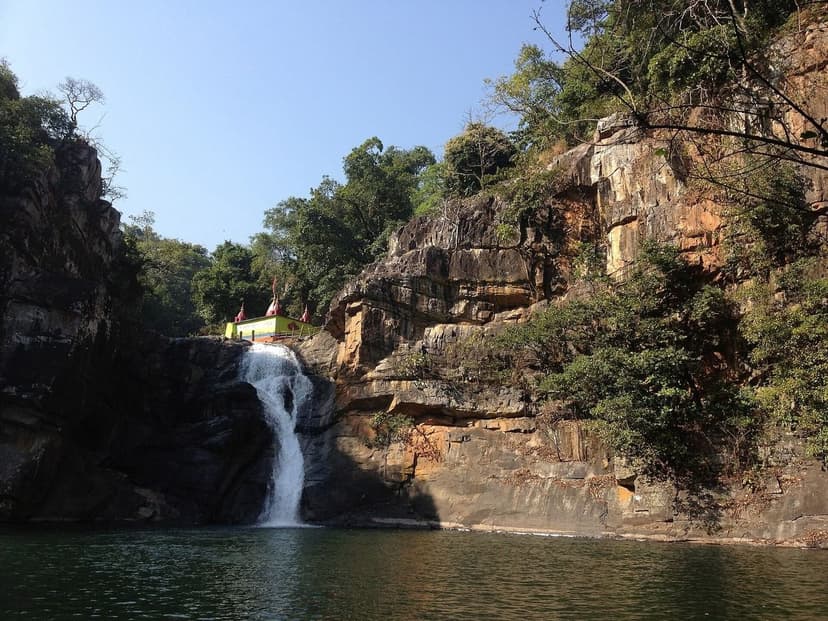 A forest waterfall dropping into a deep green plunge pool ringed by rock cliffs and trees
