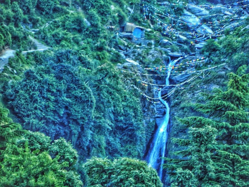 Bhagsu waterfall flowing down a forested cliff with prayer flags above Bhagsu near McLeod Ganj