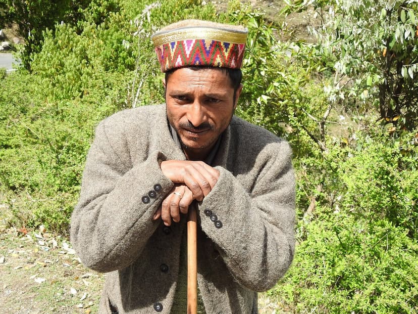 Himachali Gaddi tribe elder in traditional cap and woolen jacket leaning on a wooden staff