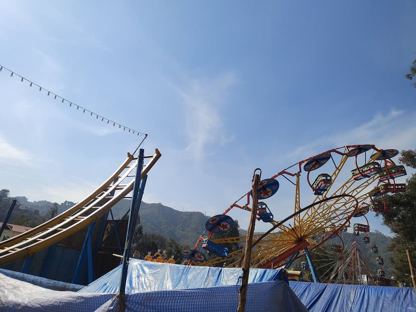 Amusement rides and a small Ferris wheel set up under string lights at Paddal ground during the Mandi Shivratri fair