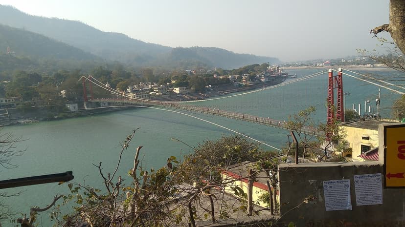 Lakshman Jhula suspension bridge spanning the green Ganga at Rishikesh with the town and forested hills behind