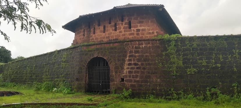 The ruined laterite bastion and arched gate of Alorna Fort in Pernem, Goa, overgrown in the monsoon