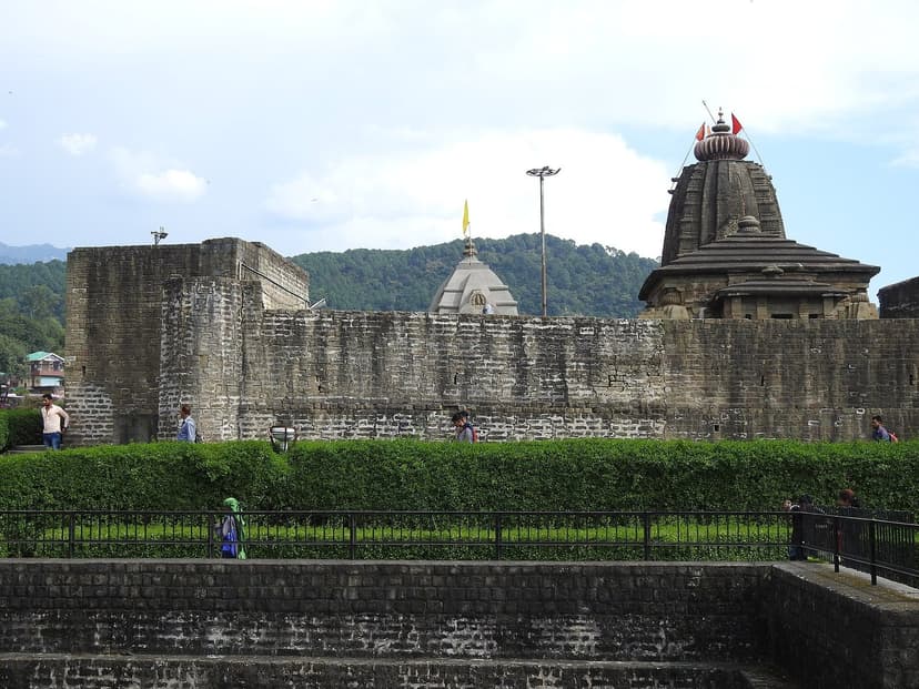 The Nagara-style stone shikhara of the Baijnath Vaidyanatha temple rising above a hedged courtyard with a yellow flag flying from a flagpole