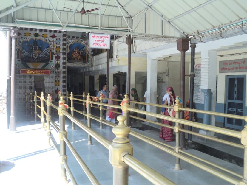 Brass-railed approach to the Main Entrance of Chamunda Devi temple in Kangra with painted murals of Shiva and Ganesha above the doorway and small clusters of pilgrims walking through