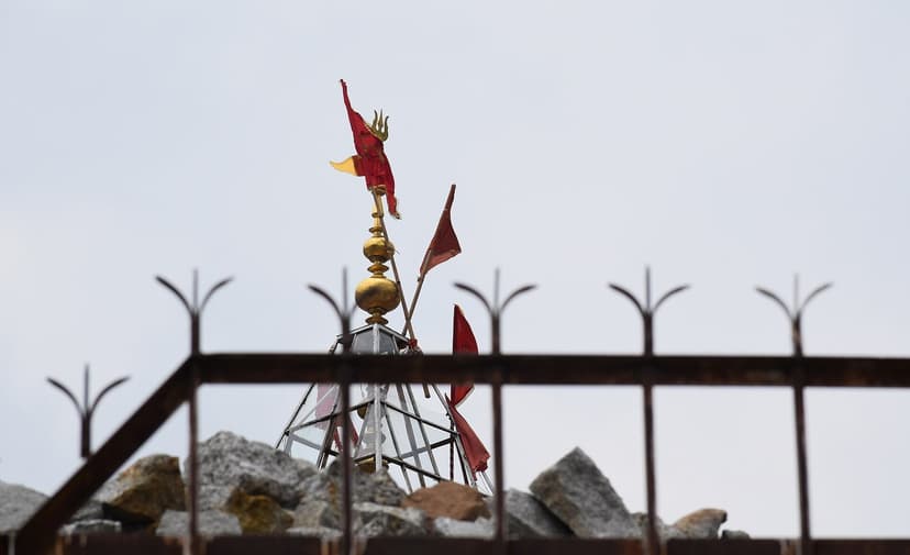 Top of Chamunda Devi Temple in Kangra district, gold finial, red prayer flags and trishul visible above the iron fence surrounding the shikhara