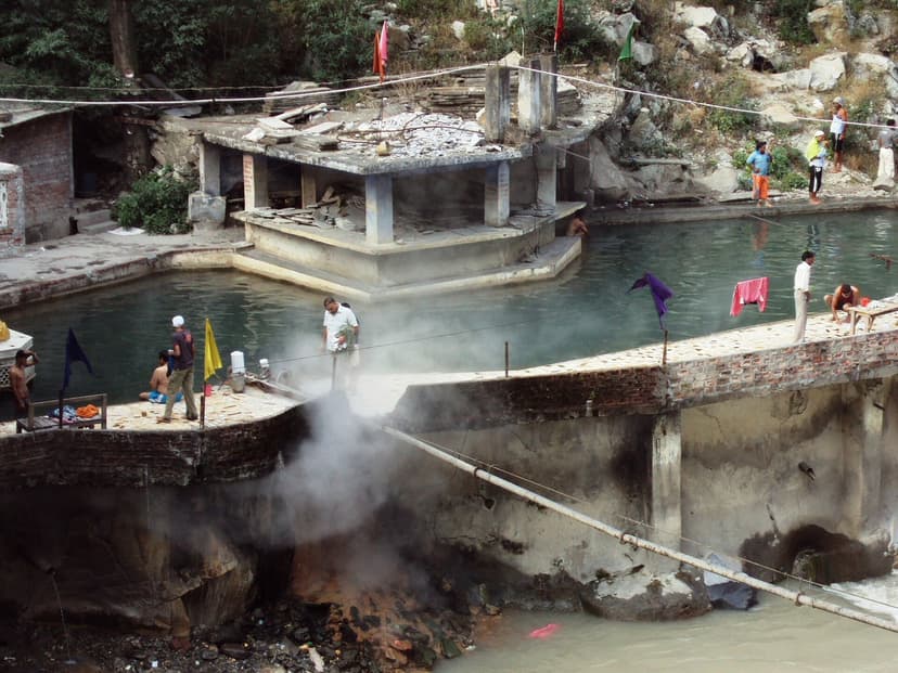 Steaming hot spring pools at Manikaran with bathers, stone platforms, river below