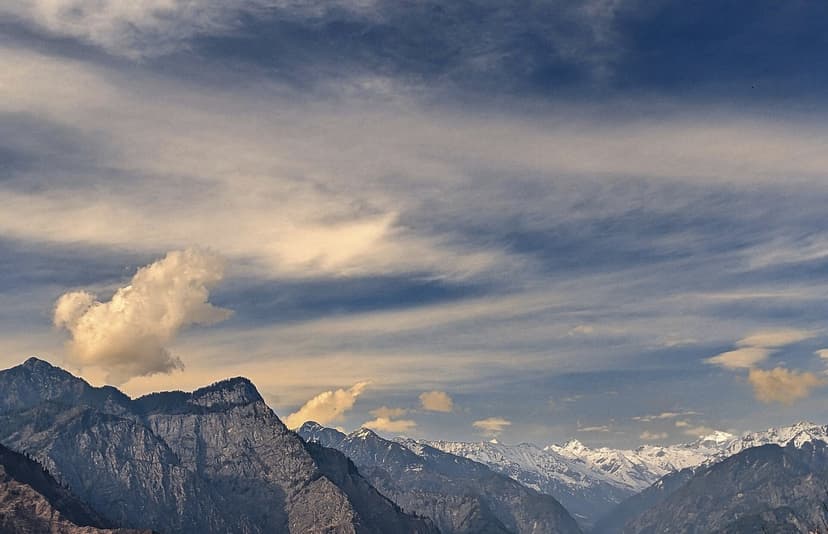 Parvati valley panorama above Kasol, layered Himalayan peaks under a dramatic cloudscape, snow line visible in the distance