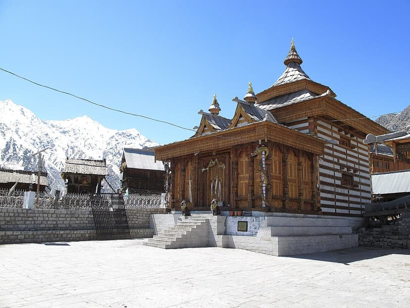 Traditional kath-kuni temple at Chitkul village in Kinnaur — alternating wood and stone construction with snow-capped Himalayan peaks behind, the last inhabited village on the Indo-Tibet road