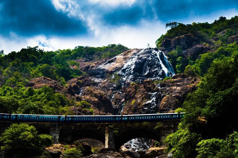 Dudhsagar waterfall in full monsoon flow with a train crossing the railway bridge below it