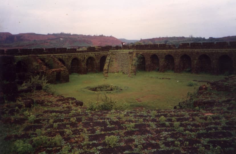 The ruined arched inner walls of Corjuem Fort around a grassy courtyard, red plateaus of Bicholim behind