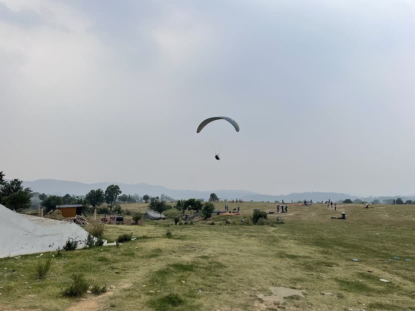 Paraglider on final approach to the Bir landing field at Chaugan with spectators on the ground