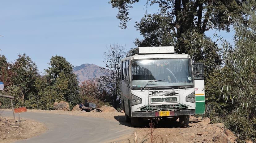 White HRTC government bus parked on a rural mountain road