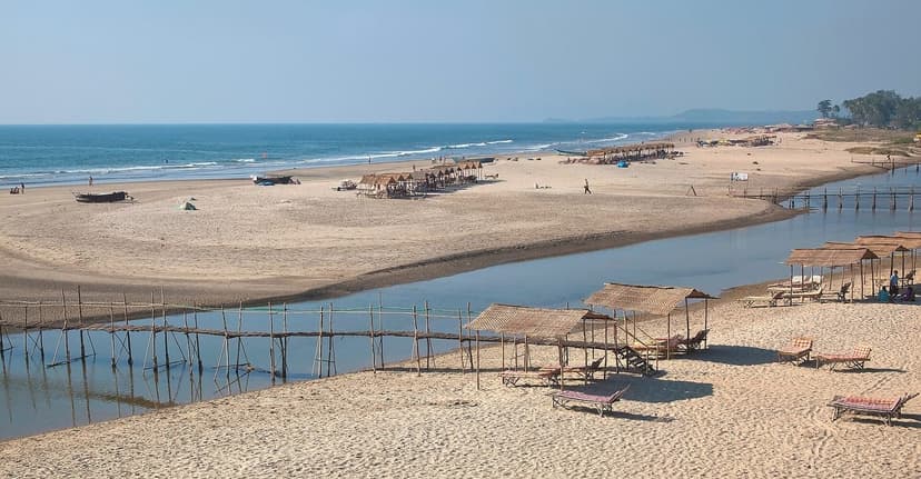 A wide, quiet Mandrem beach in North Goa with the Mandrem river backwater, bamboo footbridges and thatched loungers on the sand