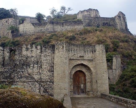 The arched stone gate of Kangra Fort with weathered sandstone ramparts rising behind