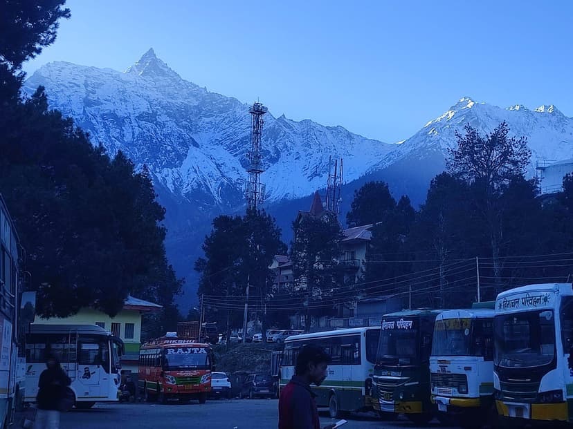 Reckong Peo bus stand at dusk with HRTC buses and the last light catching snow peaks above the town