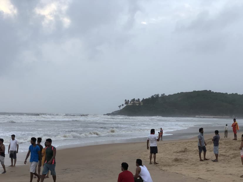 A crowd of people on busy Baga beach in North Goa with a rough sea and the headland behind