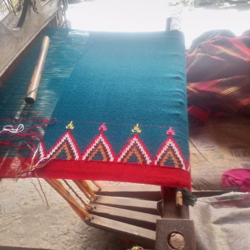 A Kullu pattu on a wooden handloom, teal weave with a red border and woven triangular temple motifs