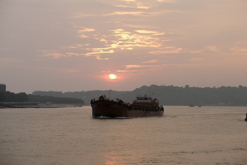 Sunset over the wide Mandovi River at Panaji with a boat silhouetted against an orange sky and forested far bank