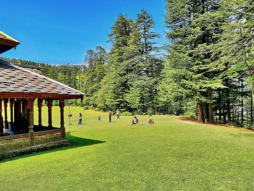 The wooden Shangchul Mahadev temple pavilion on the green Shangarh meadow under a blue sky