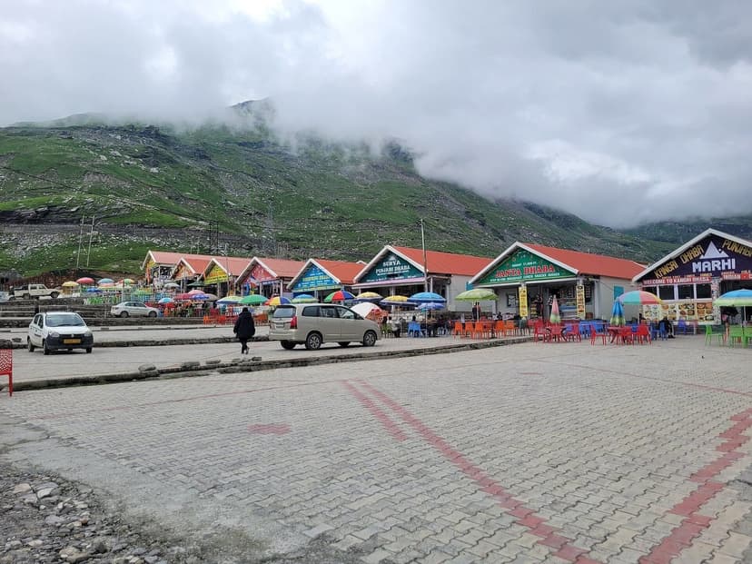 A row of dhabas with bright roofs, umbrellas and plastic chairs at Marhi, the midway halt between Manali and Rohtang Pass, under monsoon cloud