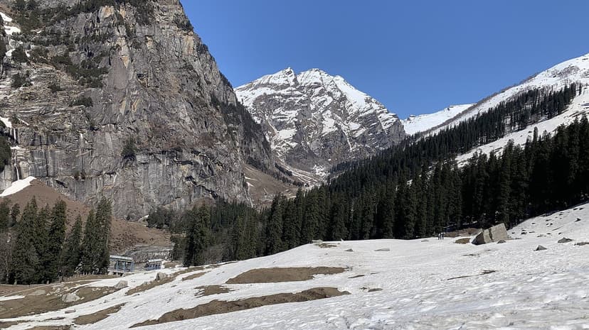 Snow-covered valley floor below rock cliffs and a peak near Sethan above Manali