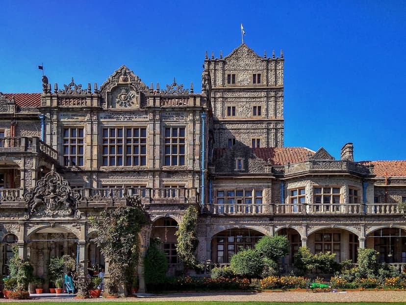 Full front facade of the Viceregal Lodge (now IIAS Rashtrapati Niwas) in Shimla — imposing Jacobean Renaissance stone building with towers, arches, manicured garden with flowers in foreground, blue sky