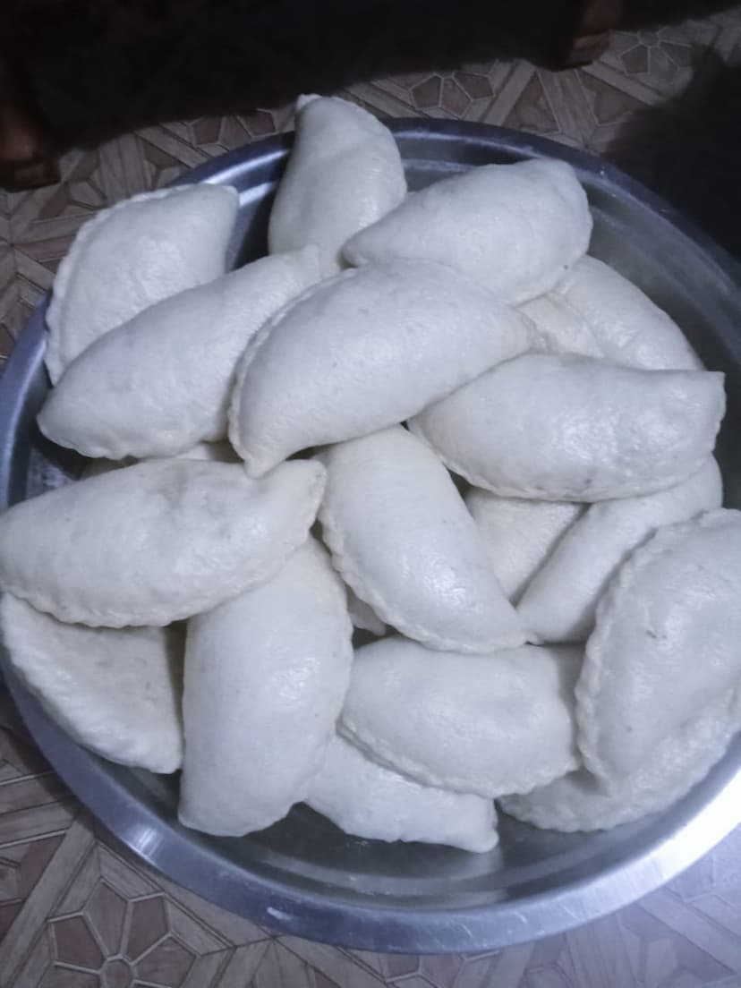 A steel plate piled with pale crescent-shaped steamed siddu, a stuffed Himachali bread, on a patterned table