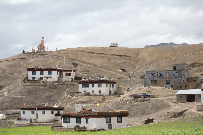 Langza village in Spiti — traditional white Spitian houses on a hillside with the golden Maitreya Buddha statue visible on the hilltop
