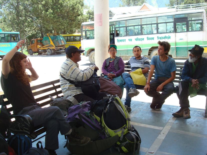 Backpackers waiting under the awning at Reckong Peo bus stand with a green HRTC bus marked Reckong Peo in Hindi behind them