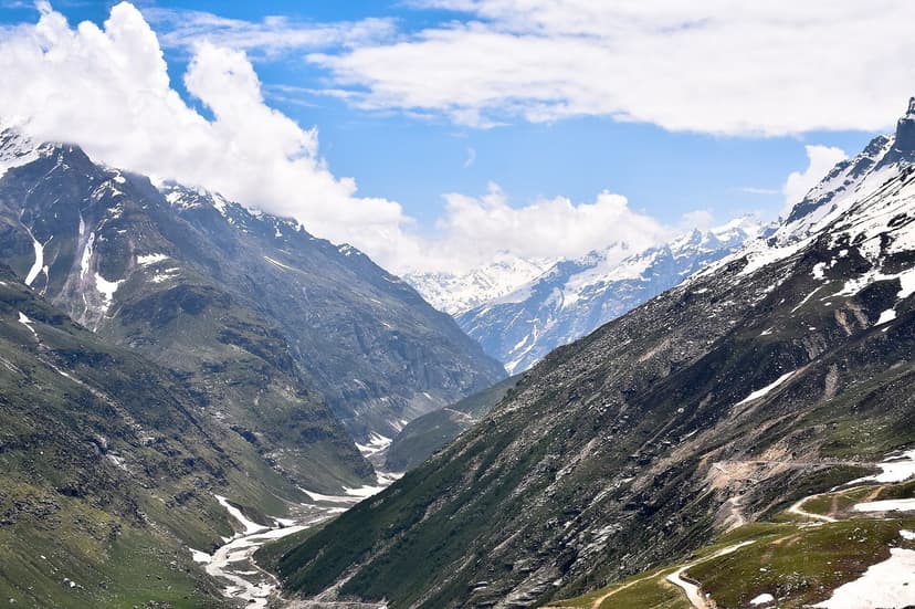 View of the Chandra valley and snow-covered mountains from Rohtang Pass area, with the winding road visible below