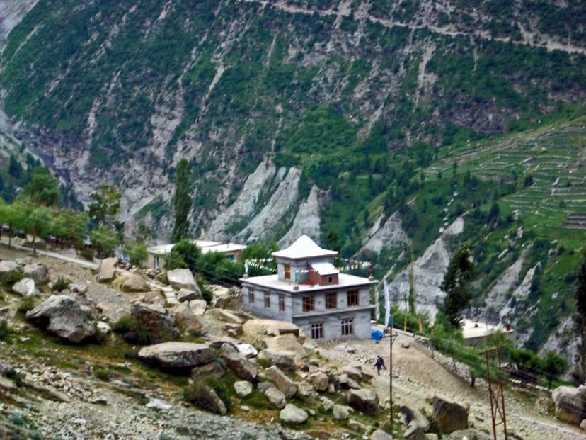 Gandhola Gompa white monastery building with red-framed windows and pagoda-style roof on a bare hillside in Lahaul, prayer flags visible in foreground