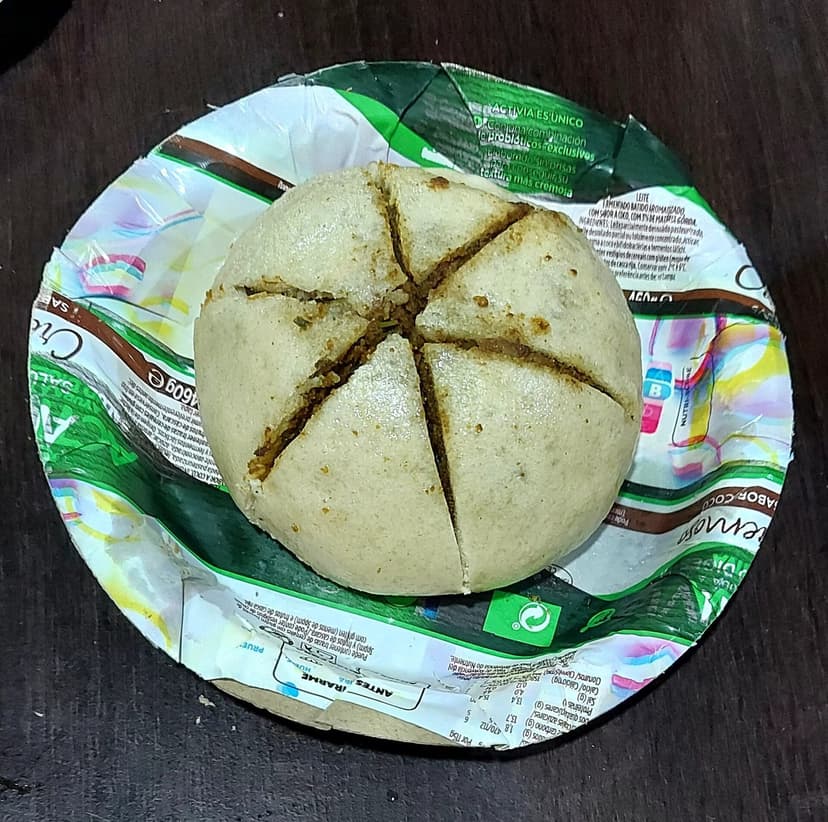 A round Himachali siddu, a soft, white, steamed wheat bread cut into a star pattern, sitting on a paper plate with the dark filling visible in the cuts